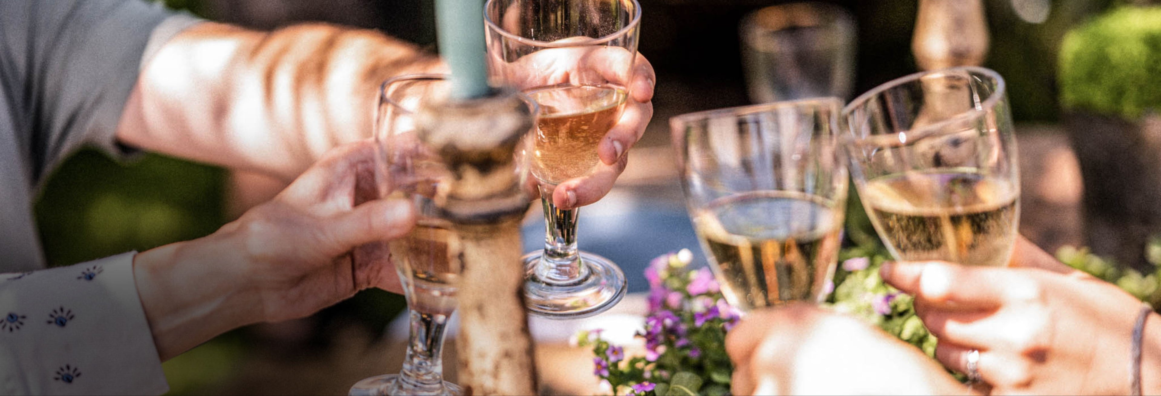 Outdoor setting with flowers, a glass, and small bowls on a wooden surface, with people dining.