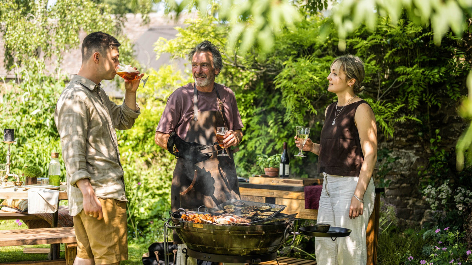 Three people enjoying a Kadai barbecue outdoors in a garden setting.