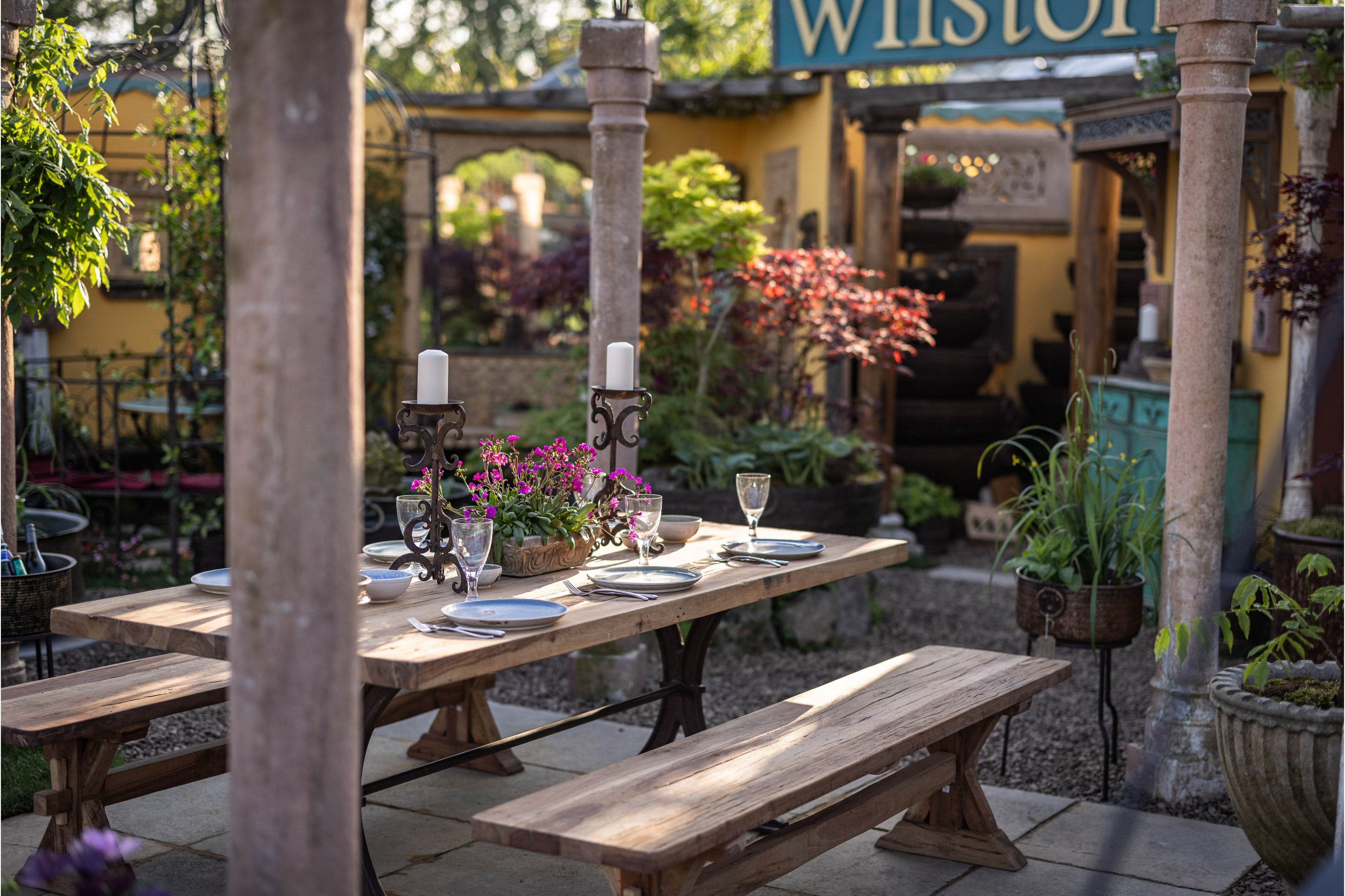 Outdoor wooden table in a garden setting with plates and cutlery laid out.