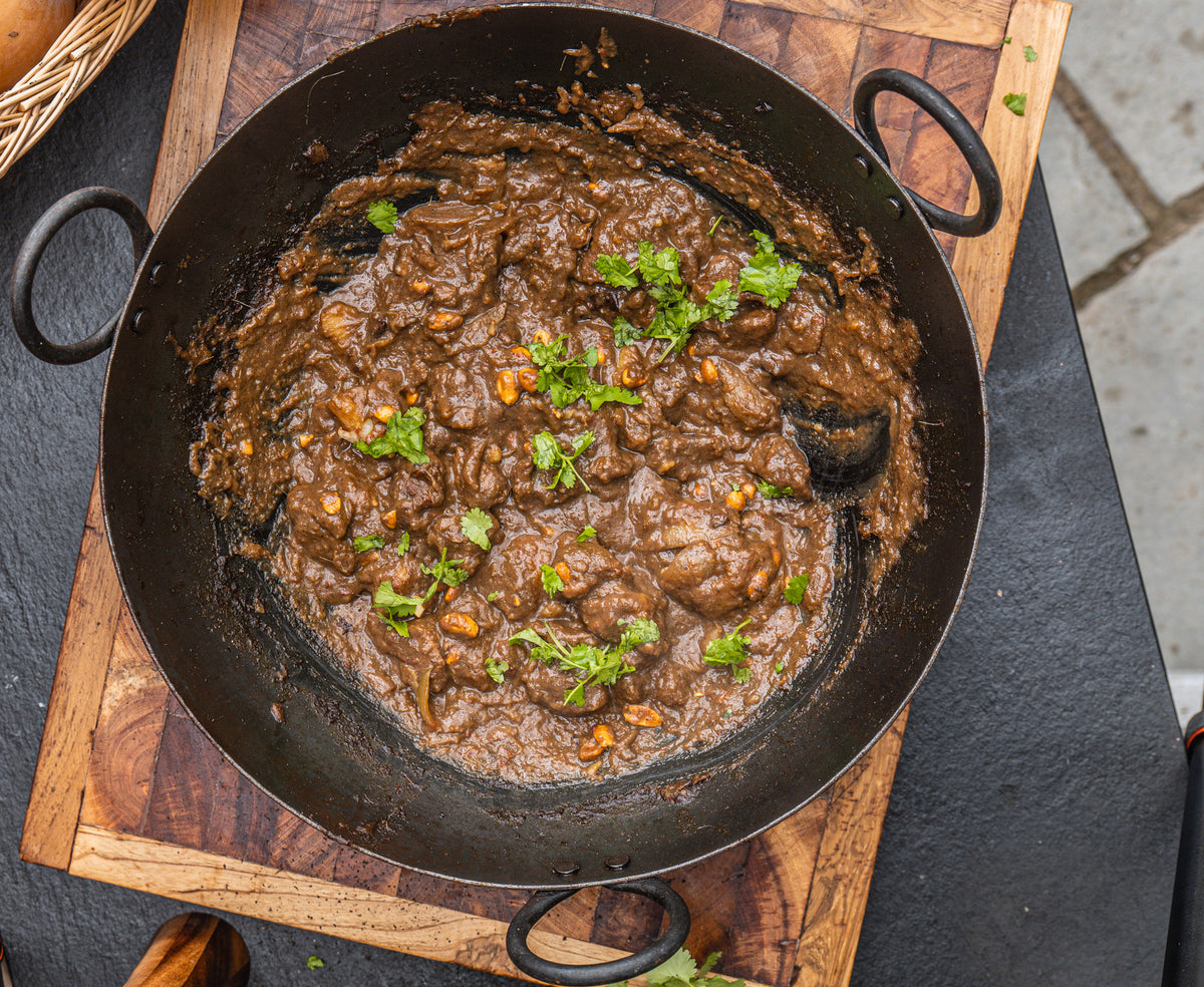 a cooking bowl full of venison massaman curry on a large wooden chopping board. The curry is topped with coriander and peanuts.
