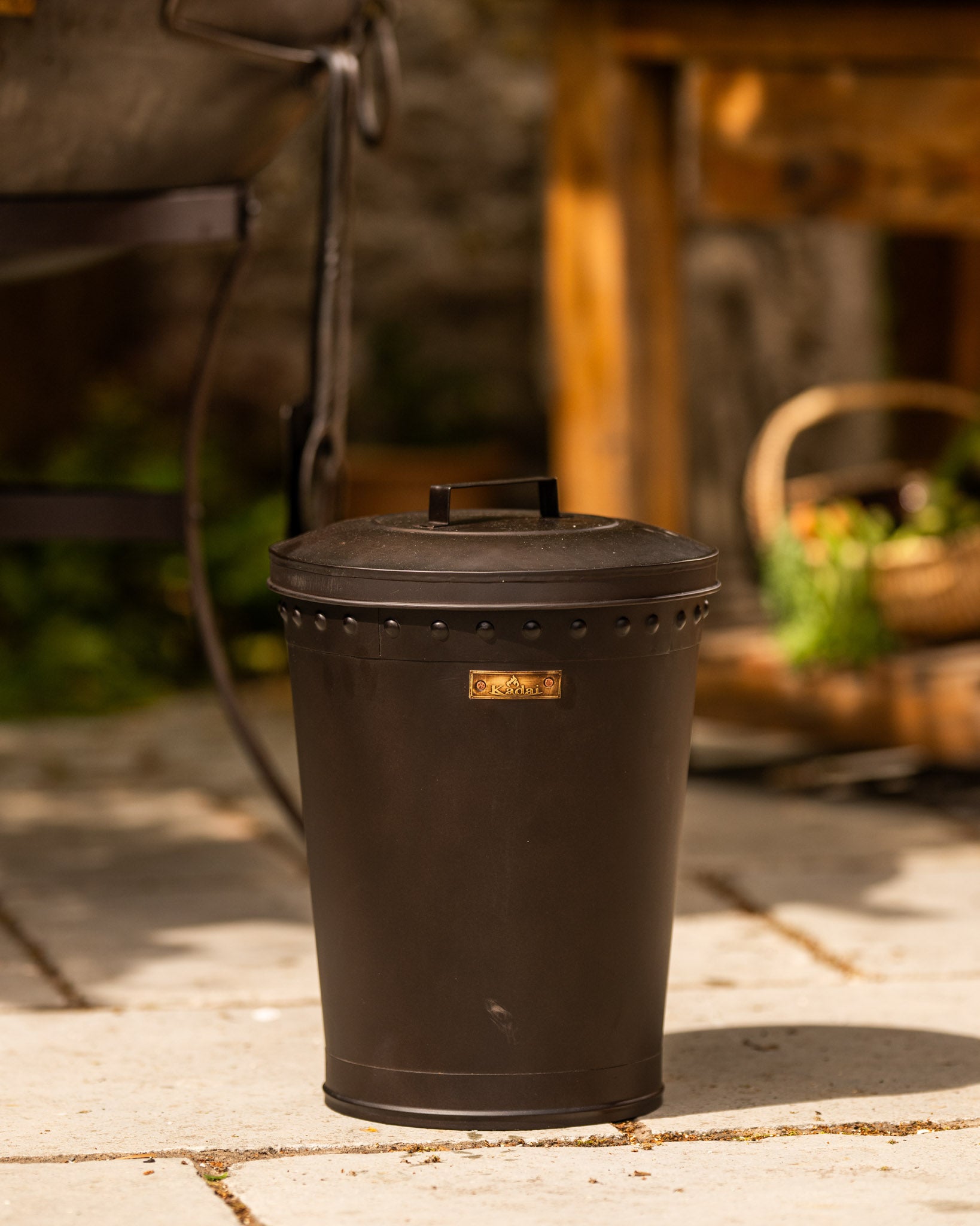 Black BBQ bin with fitted lid beside a Kadai firebowl barbecue in an outdoor garden cooking space