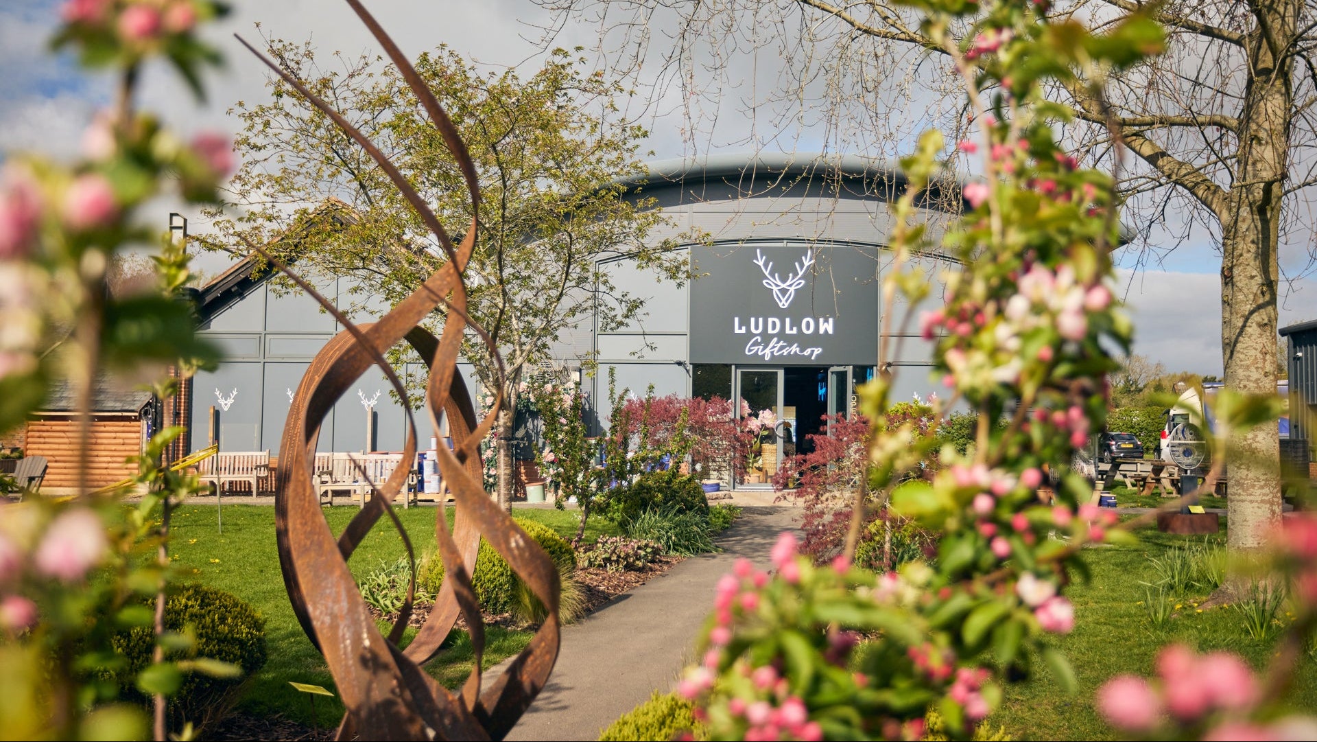 Ludlow Farm Shop building with decorative metal sculpture and flowers in foreground