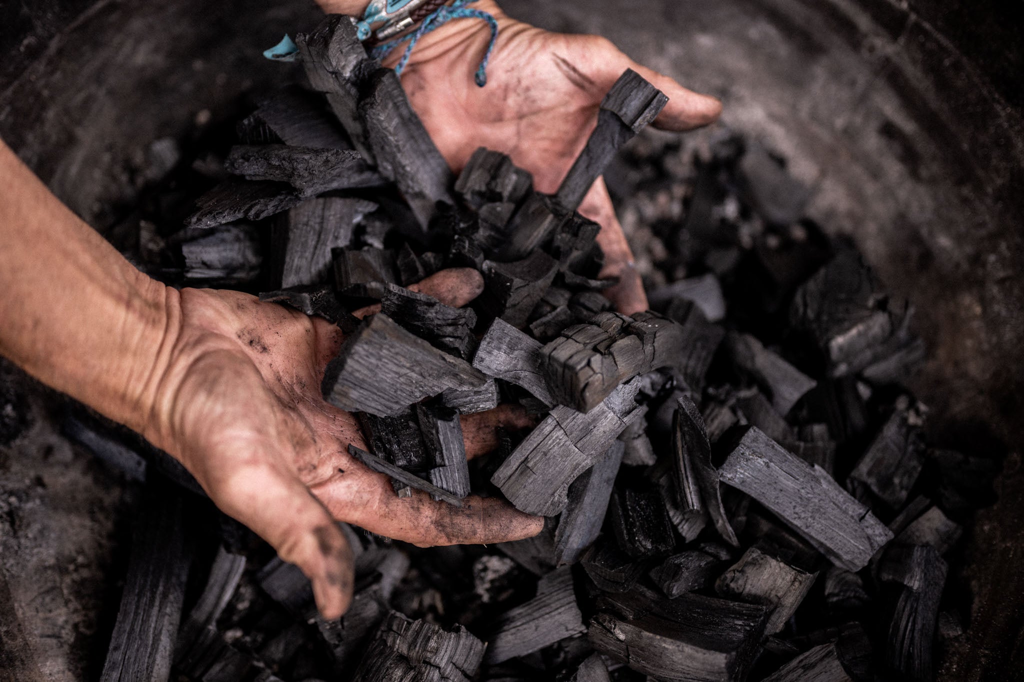 Hands holding a pile of black charcoal briquettes.