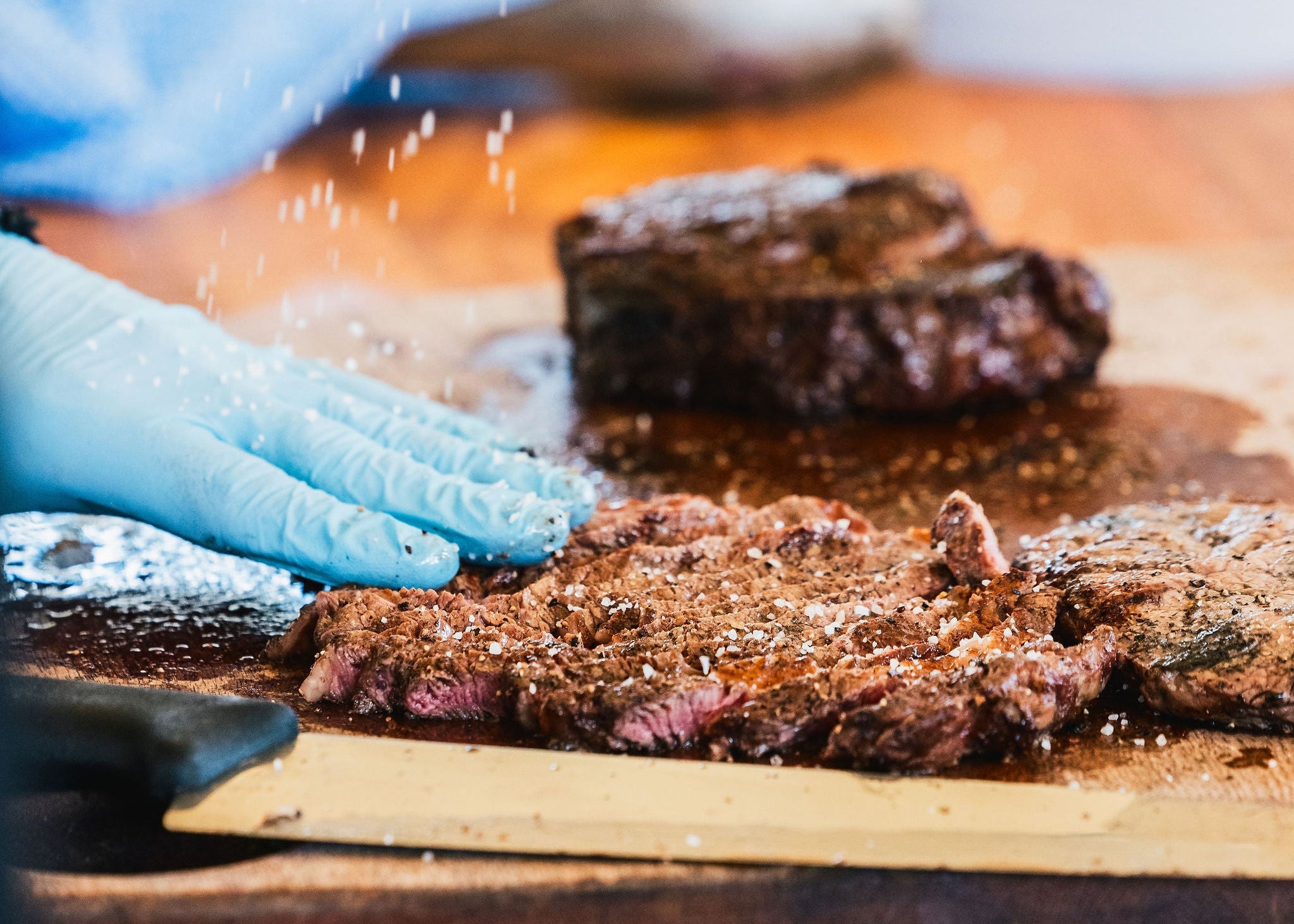 Person seasoning beef on a wooden cutting board with a blurred background