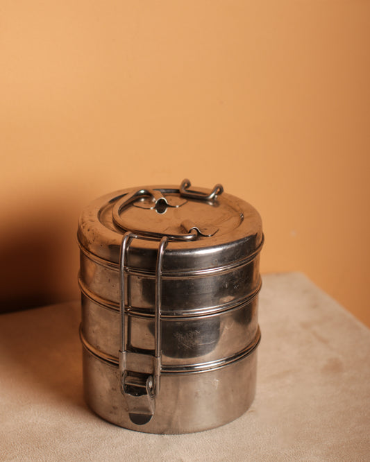 Stacked stainless steel tiffin tin on a beige surface with a warm orange background.