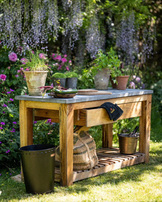 Wooden garden kitchen table with plants and tools in a lush garden setting