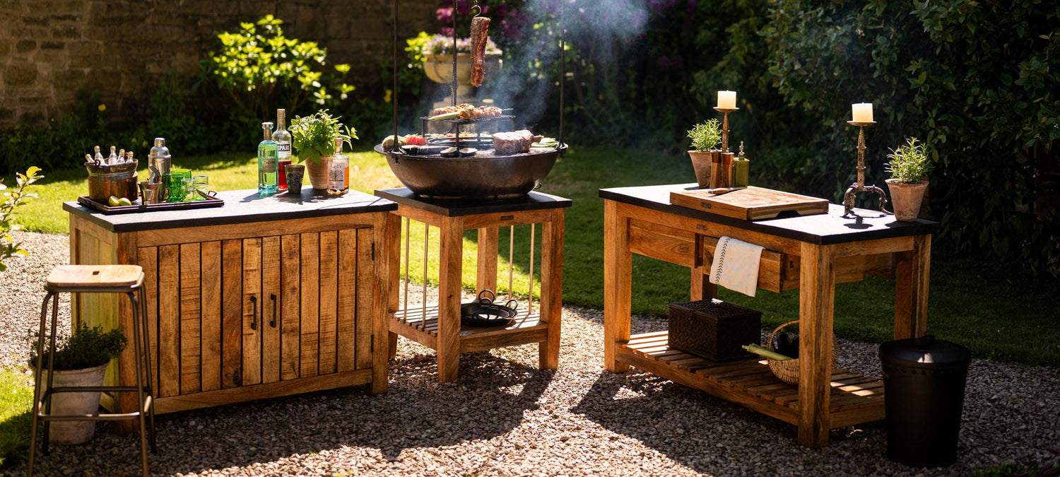 Outdoor cooking setup with wooden tables and grill in a garden.