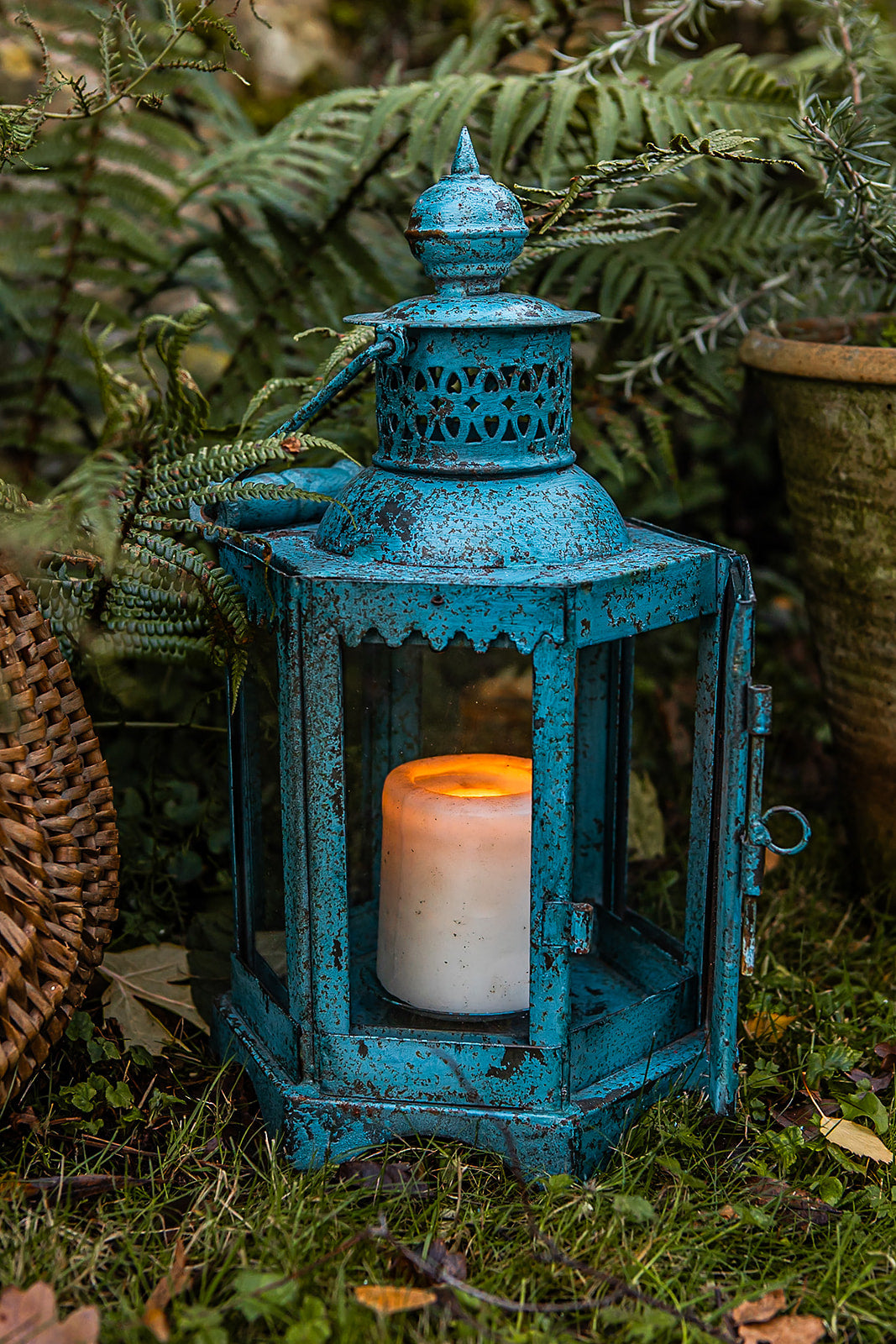 Blue lantern with a lit candle inside, surrounded by greenery