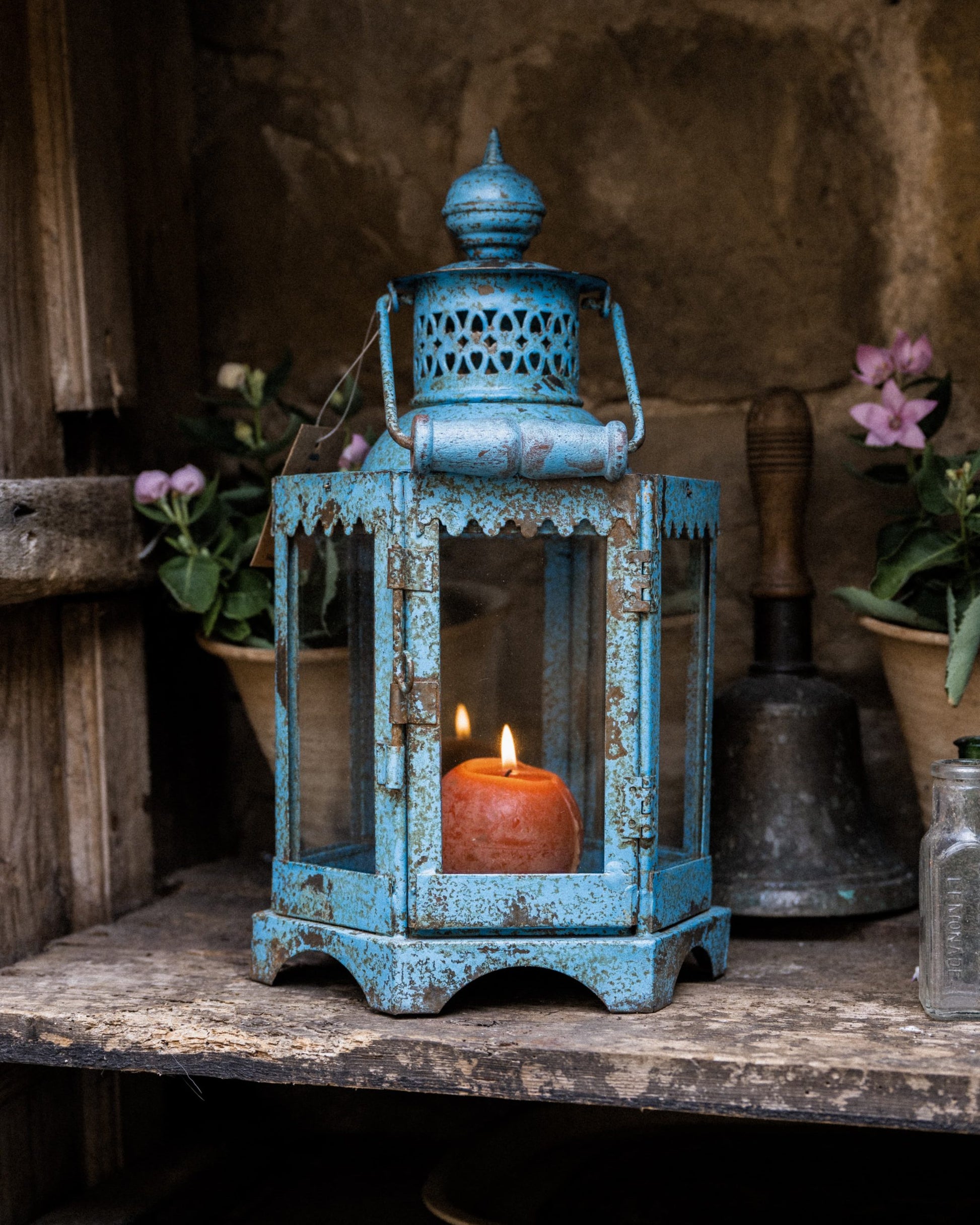 Blue lantern with a candle inside on a rustic wooden surface with plants in the background