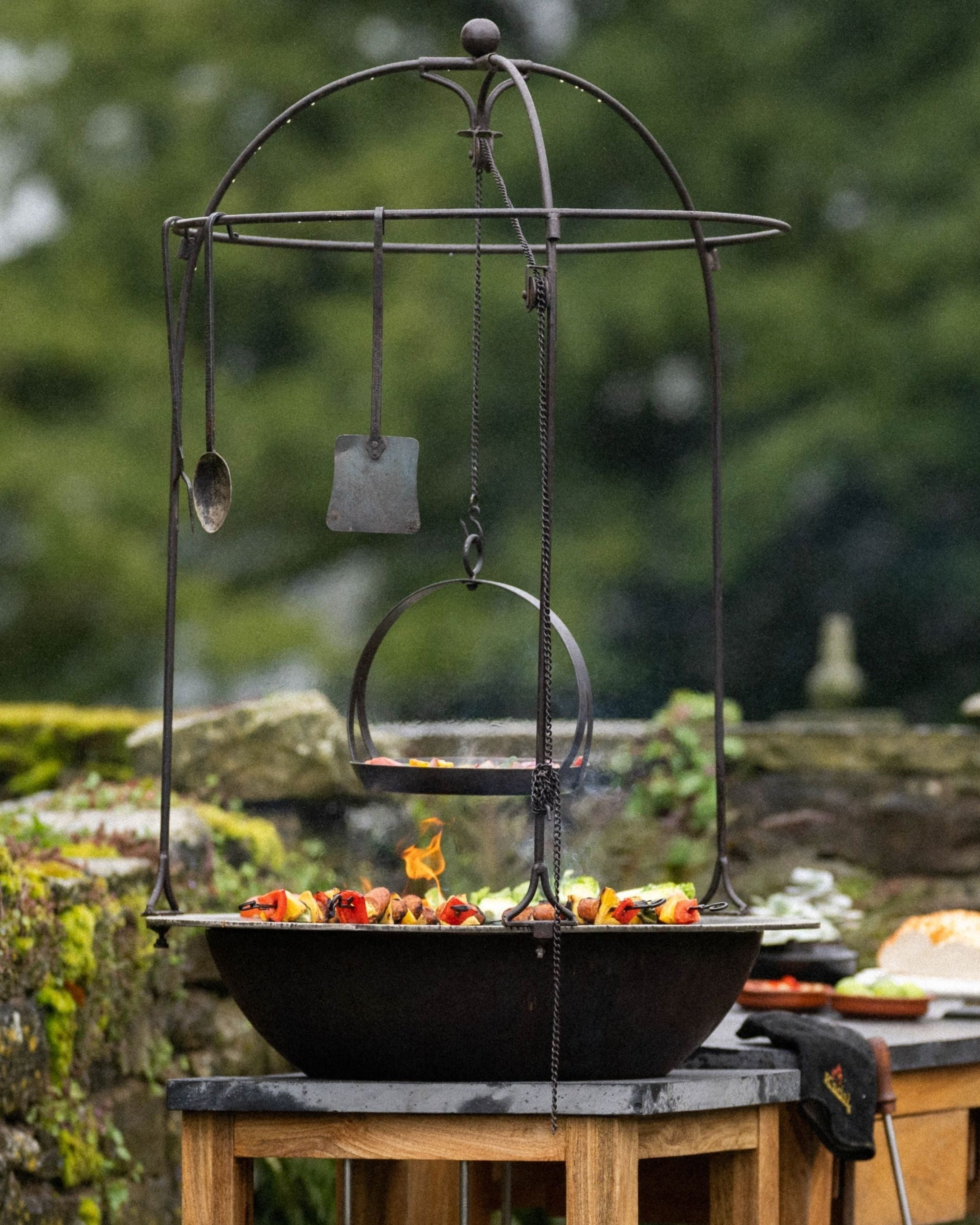 Outdoor setting with a hanging metal pot and cooking utensils.