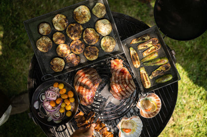 Grilled vegetables and meats on a kadai barbecue grill with a focus on the food.