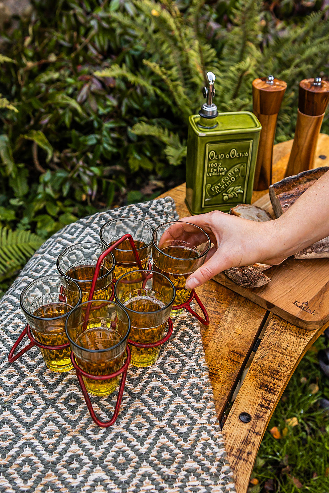 Set of chai glasses in red metal holder on outdoor table as hand serves a glass