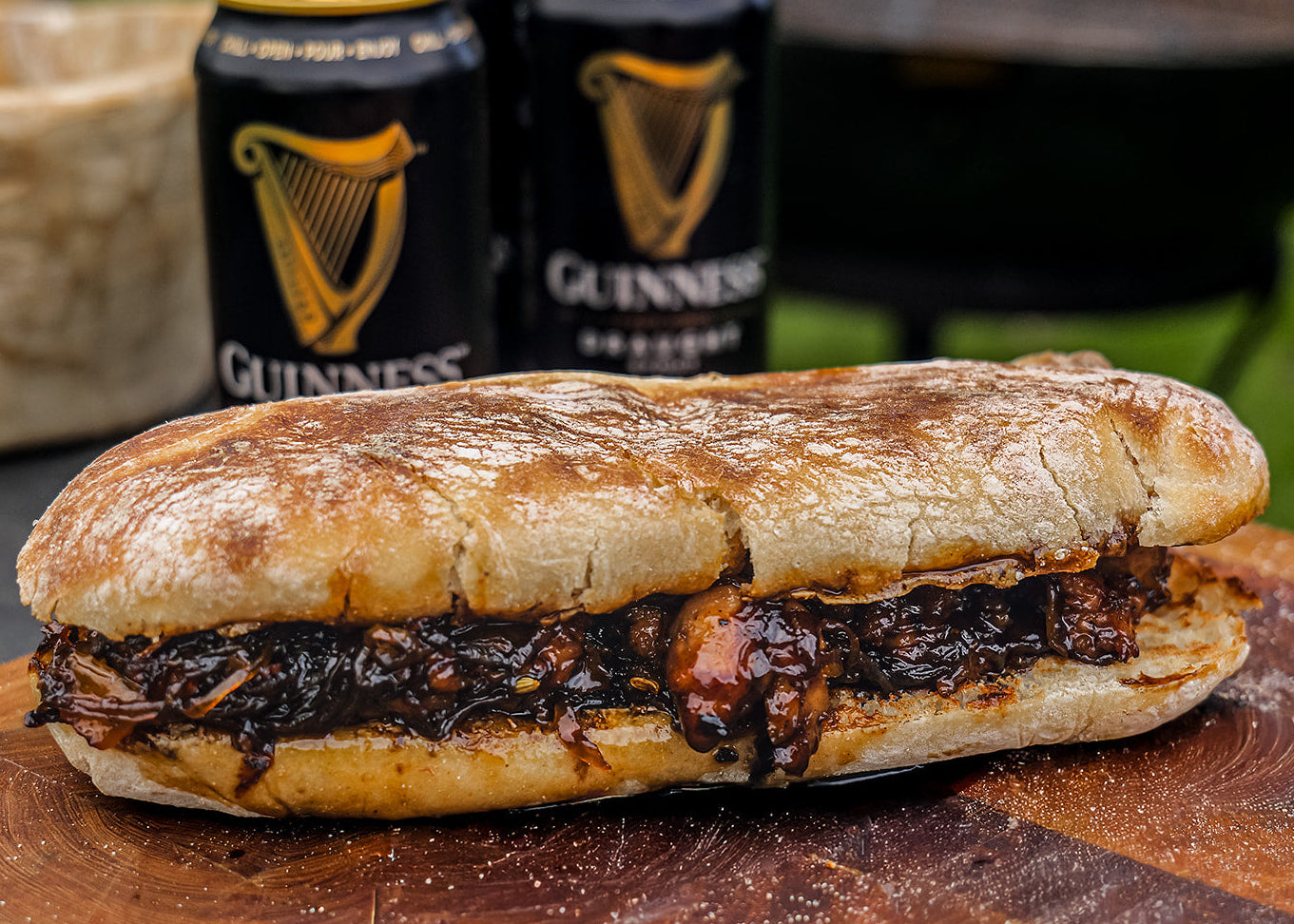 Sandwich on a wooden cutting board with Guinness beer cans in the background
