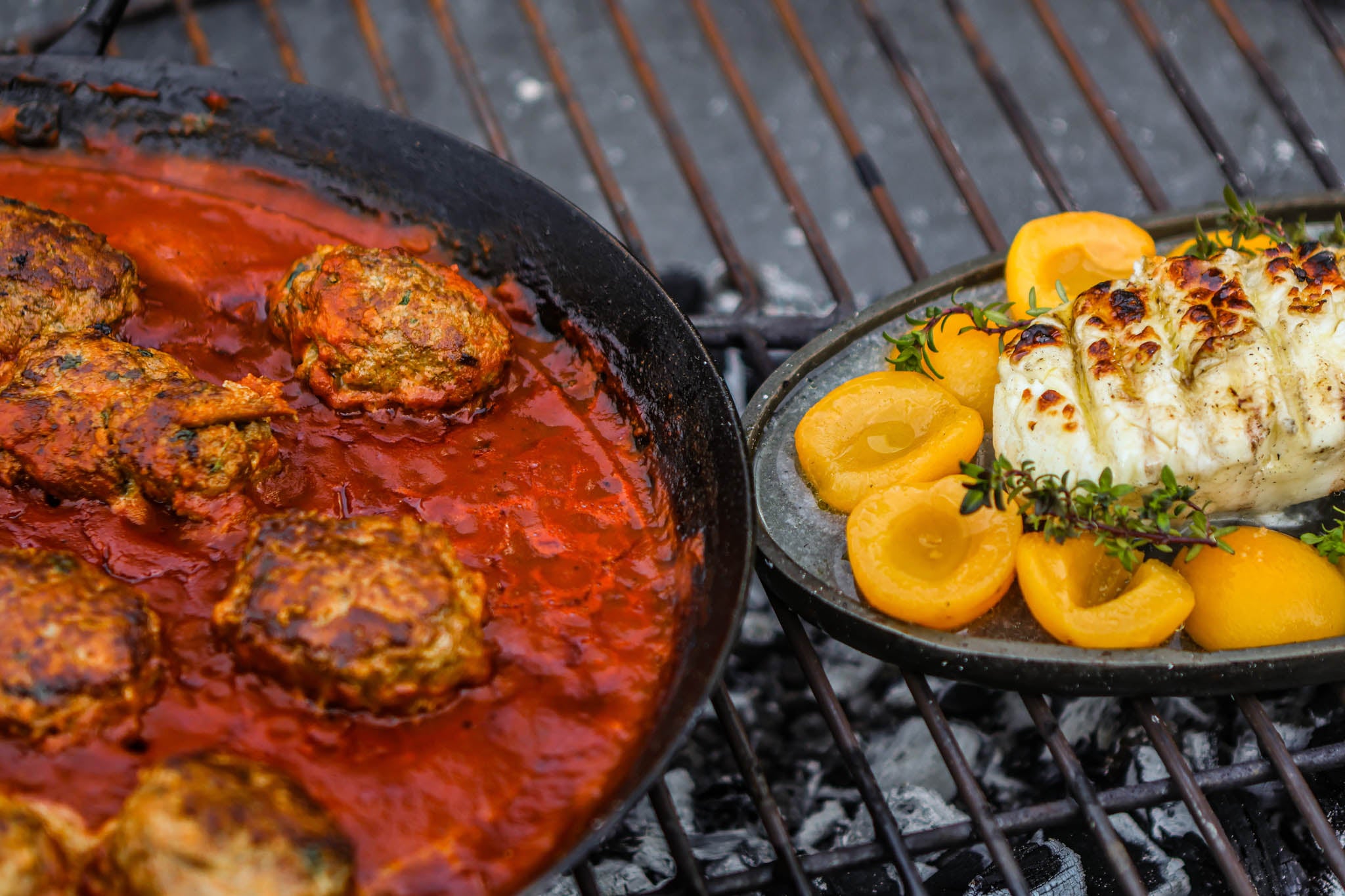 Grilled dishes on a barbecue grill including meatballs in red sauce and roasted vegetables.