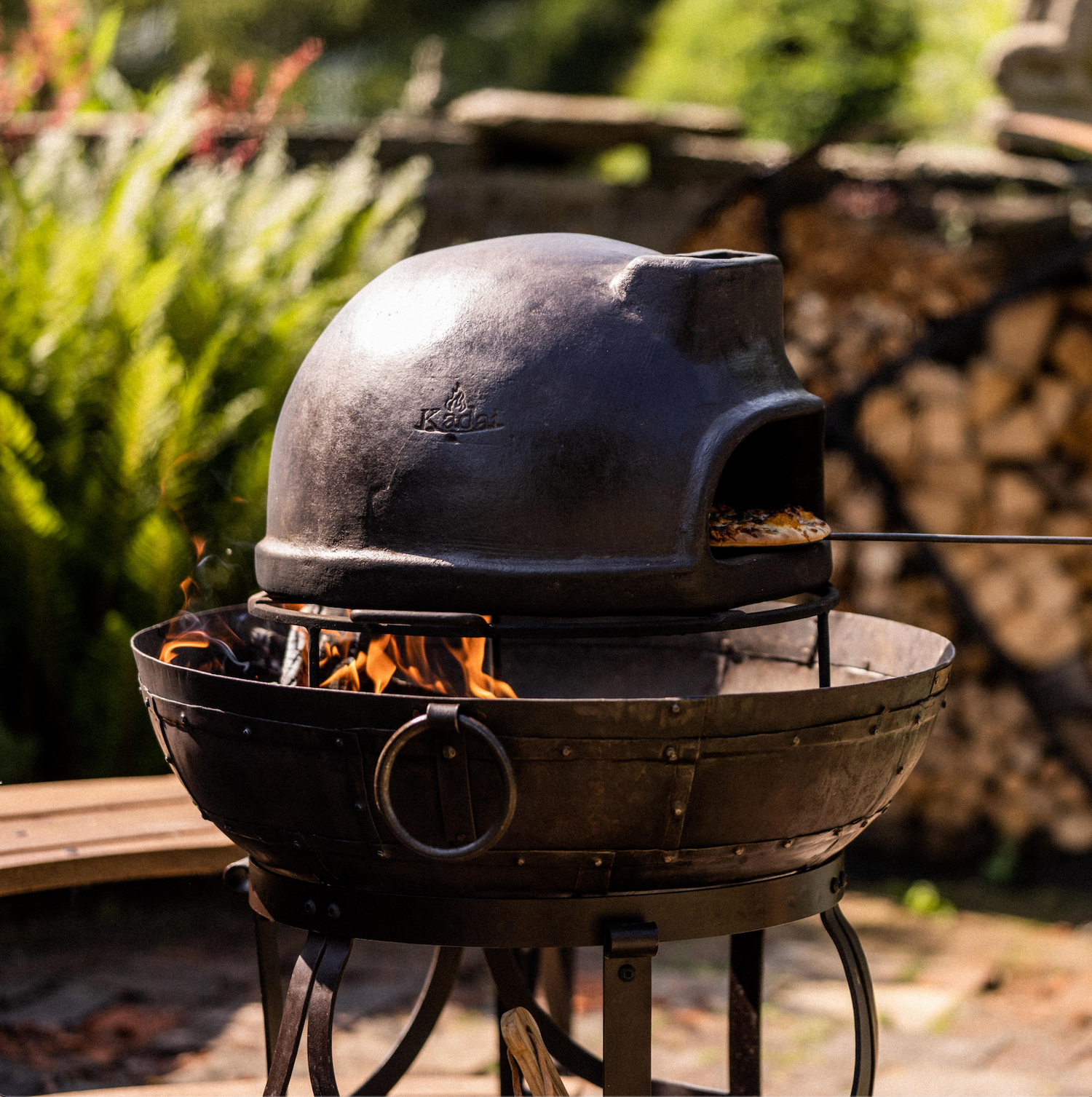 Black outdoor Kadai pizza oven with flames inside, set against a natural background.