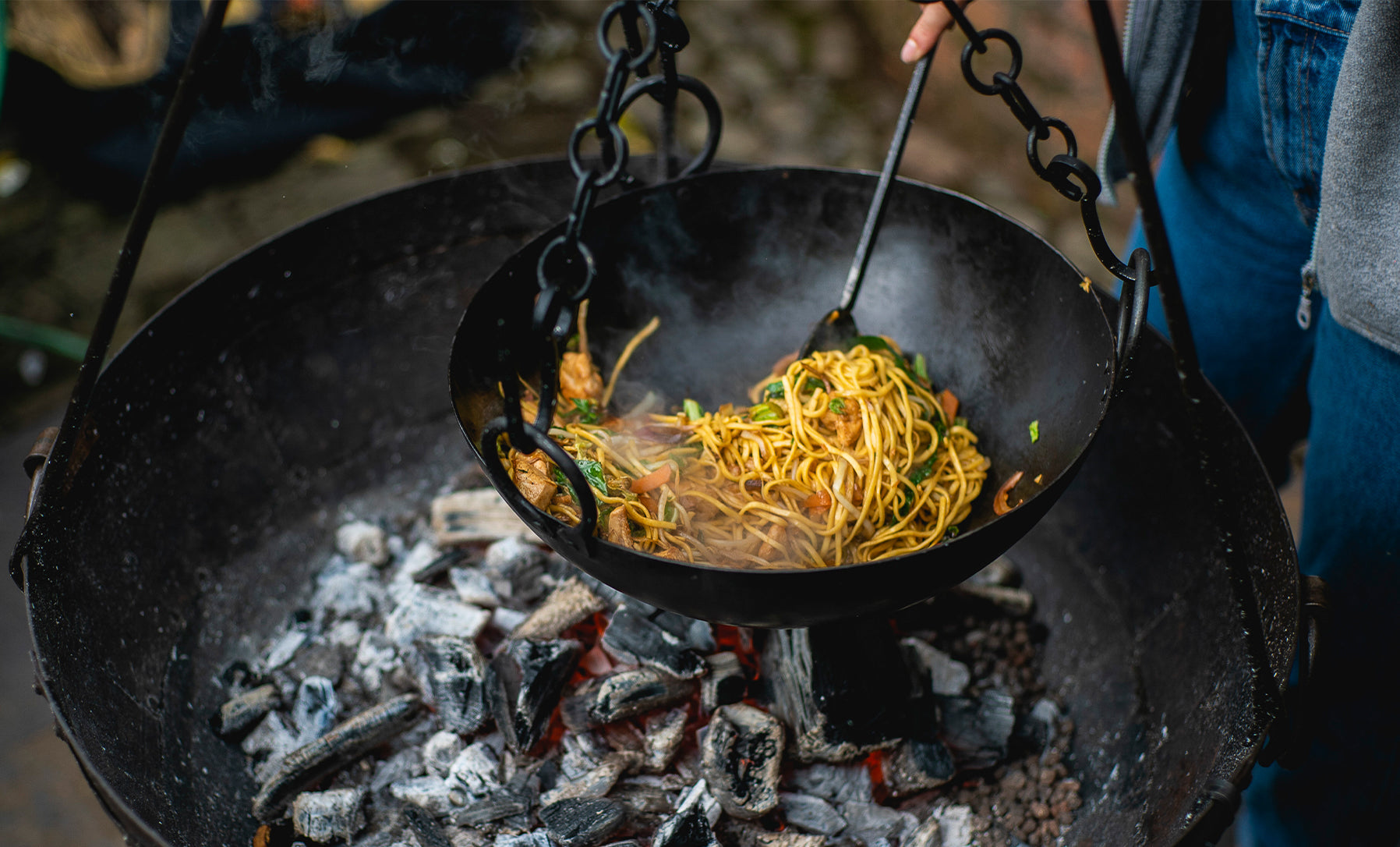 Wok with noodles in a kadai cooking bowl over an open fire