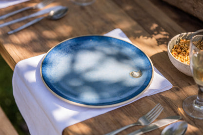 Blue ceramic plate on a wooden table with cutlery and a glass.
