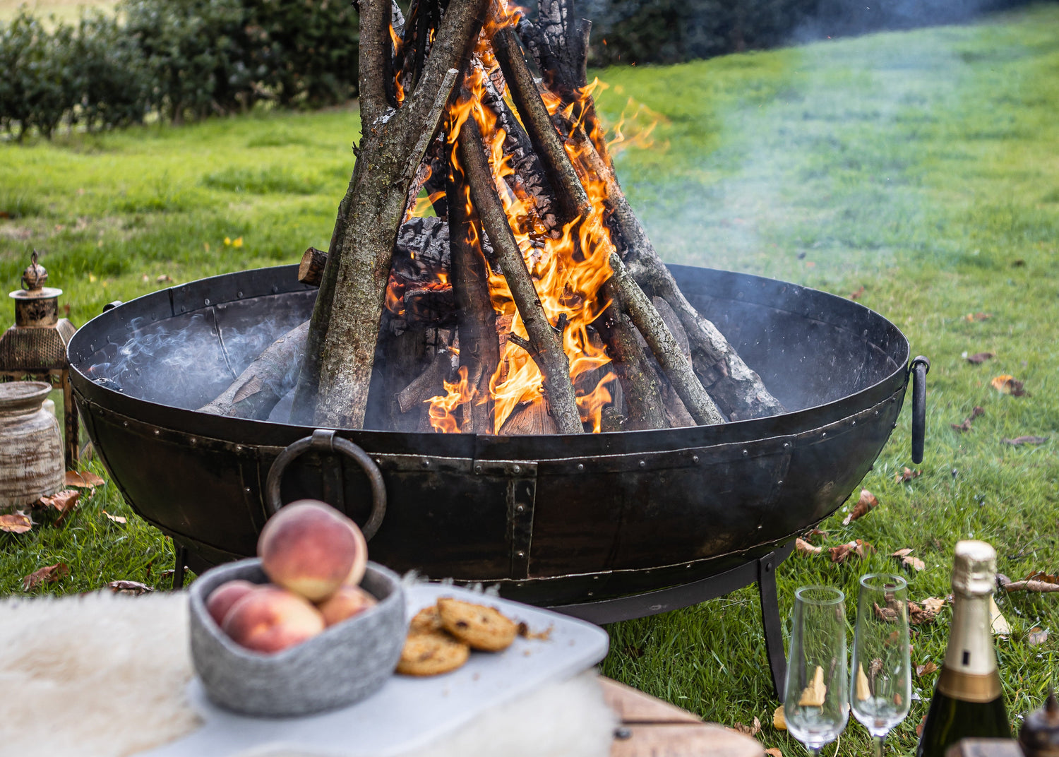 kadai Fire pit with burning wood in a grassy outdoor setting