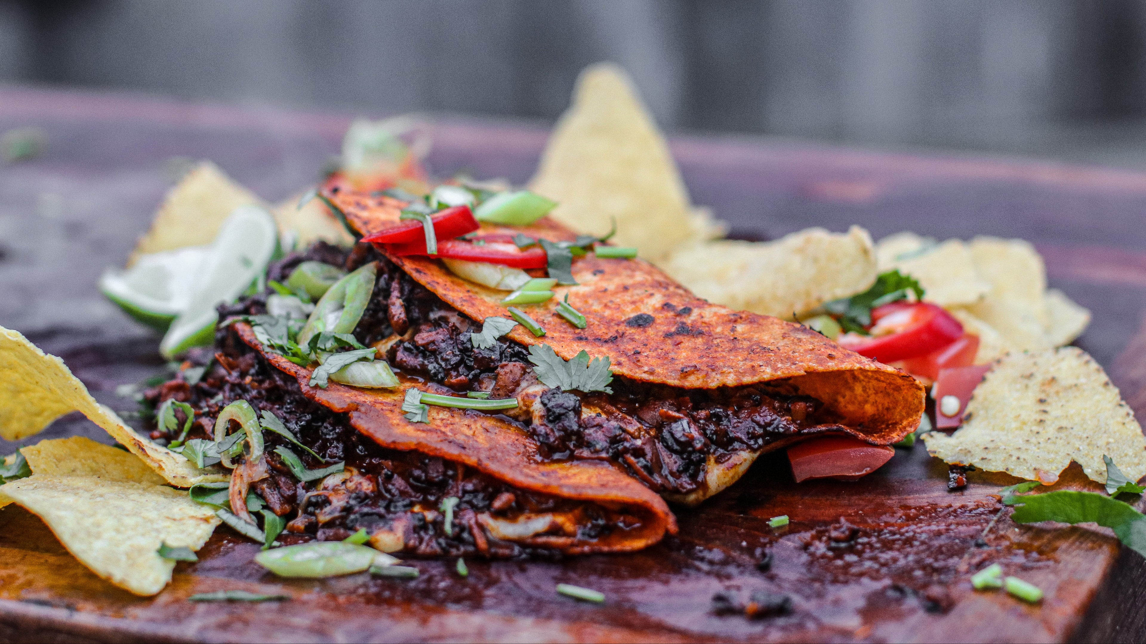Plated dish with tortilla chips and tofu birria tacos on a wooden board.