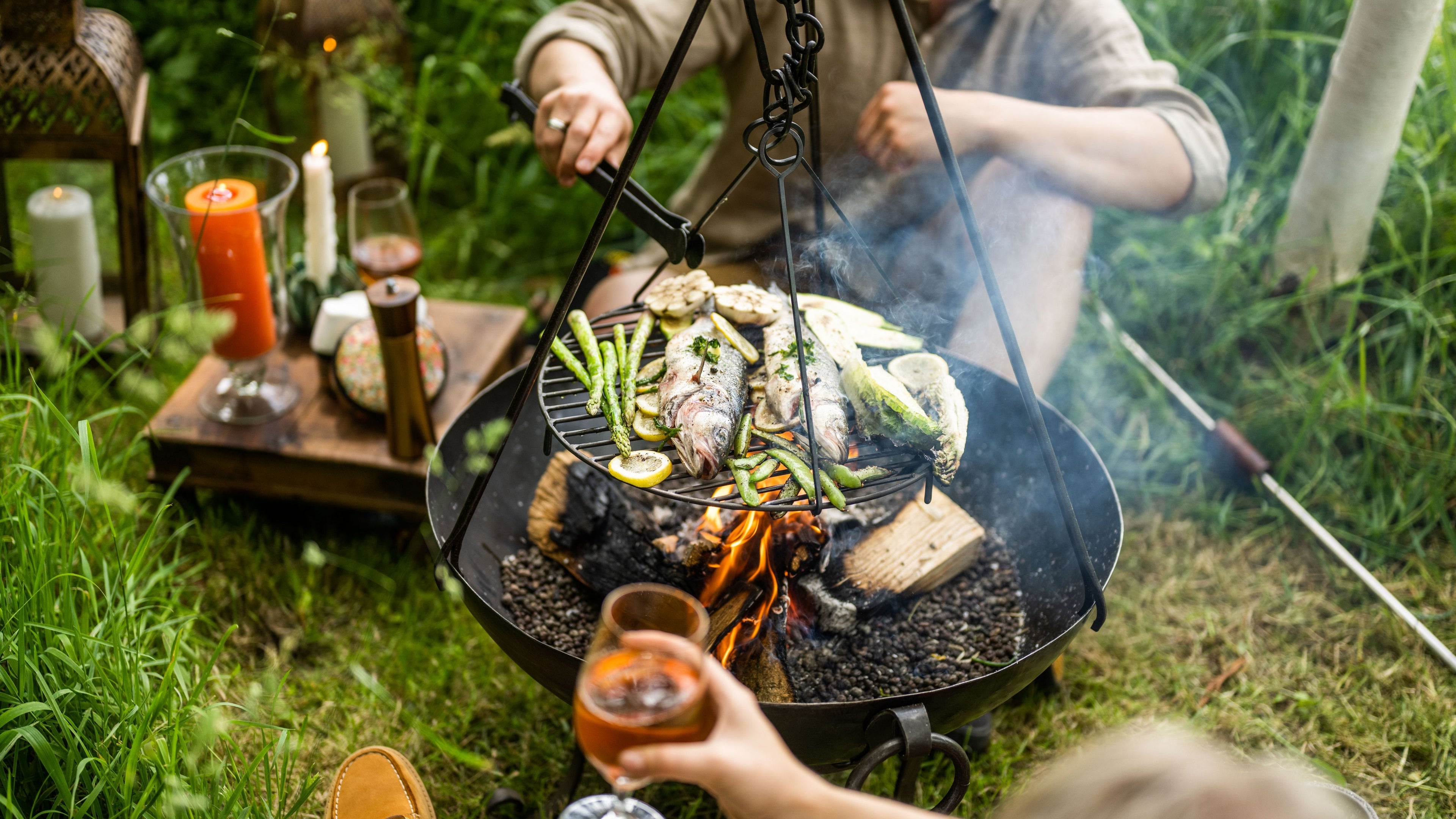 People grilling whole fish over fire on a fire pit.