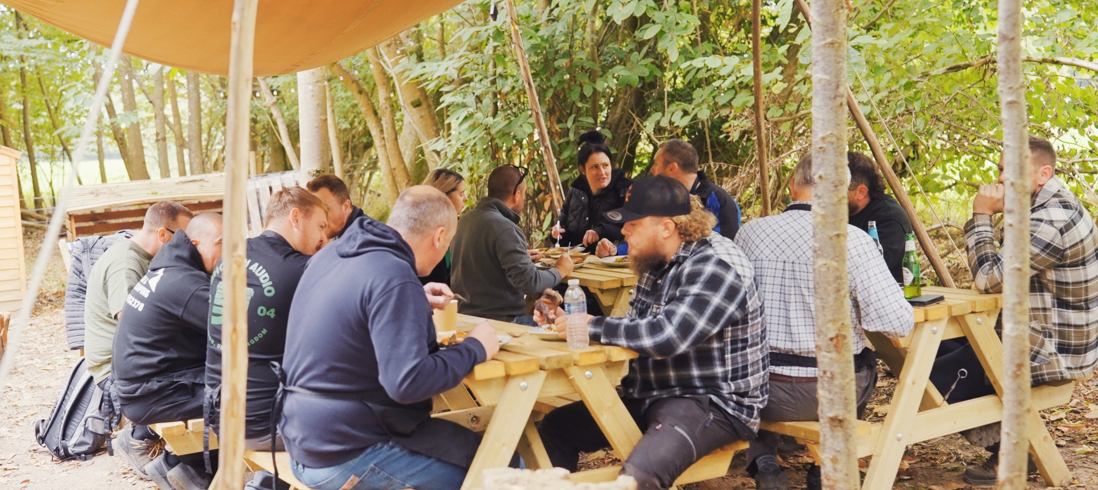 Group of people sitting around wooden tables in a forest setting