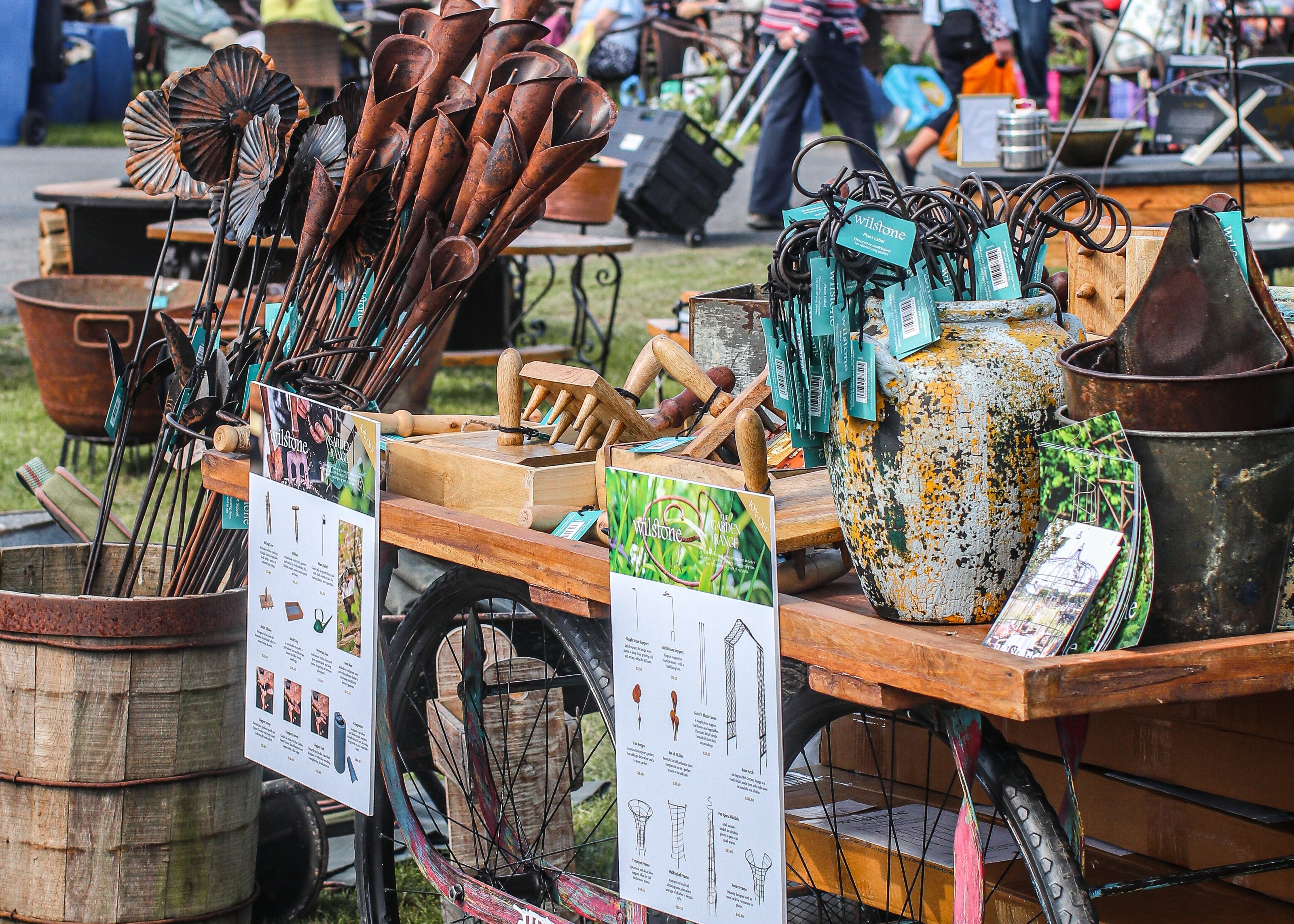 Vintage garden tools and decor on an old cart at an outdoor market.
