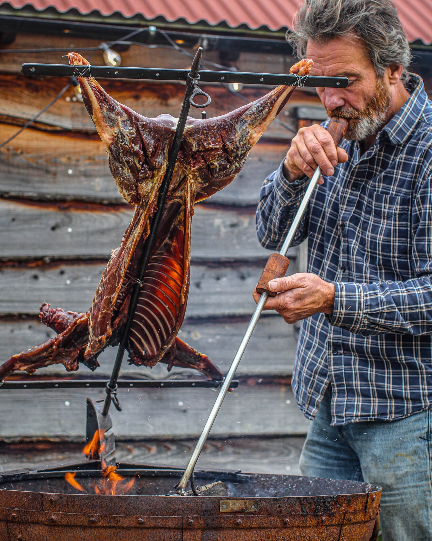 Traditional Argentine-style asado cooking with a whole lamb mounted on a metal cross over outdoor flames