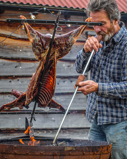 Traditional Argentine-style asado cooking with a whole lamb mounted on a metal cross over outdoor flames