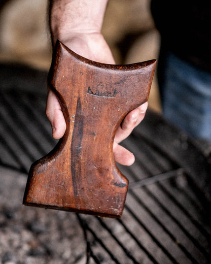 Wooden grill scraper being held above a barbecue grill grate outdoors