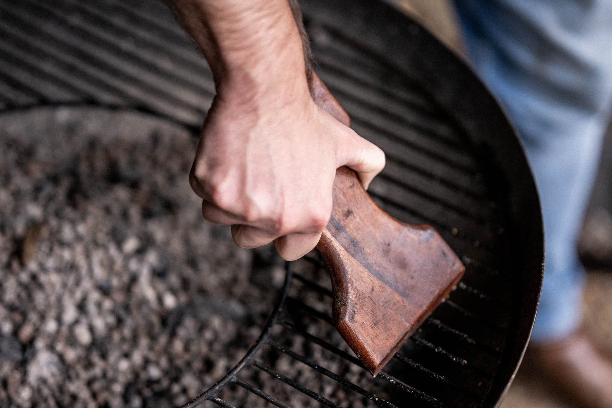 Ergonomic wooden BBQ grill scraper removing residue from a Kadai fire bowl grill without wire bristles