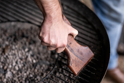 Ergonomic wooden BBQ grill scraper removing residue from a Kadai fire bowl grill without wire bristles