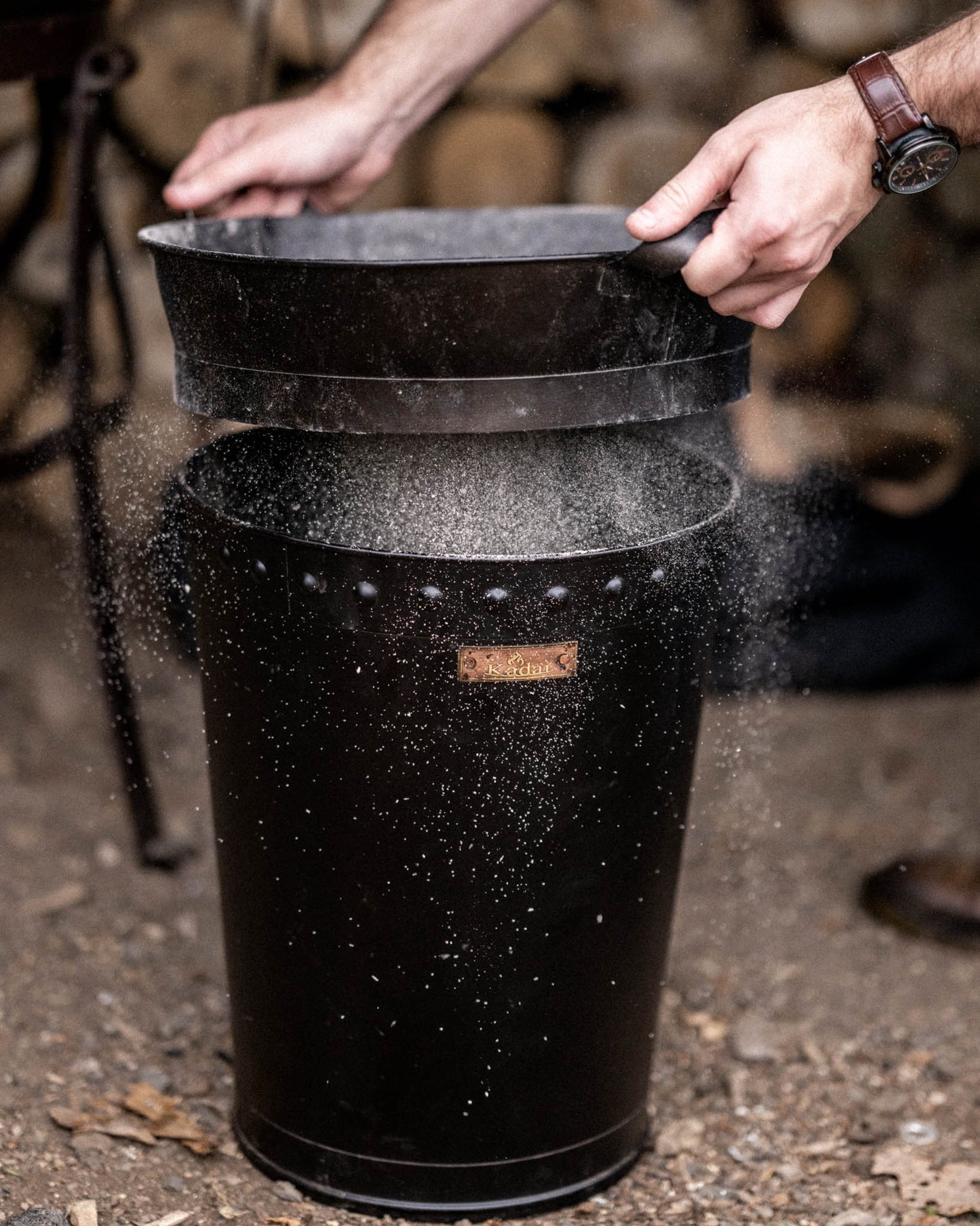 Black BBQ bin with ash sifter attachment removing charcoal dust and ash in an outdoor barbecue setting