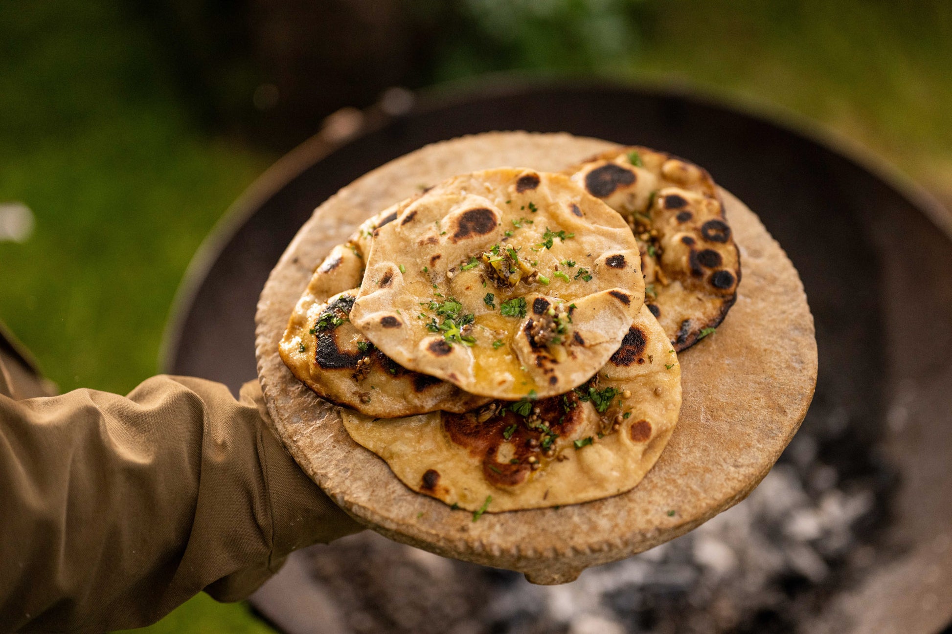 Person holding a sand stone board with flatbreads over a campfire