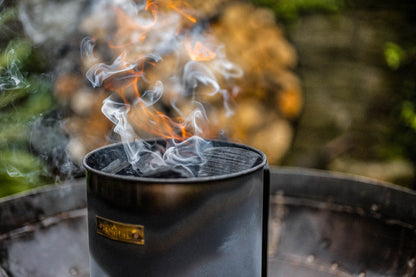 Smoking charcoal starter with glowing embers igniting inside a metal chimney for barbecue and fire pit cooking