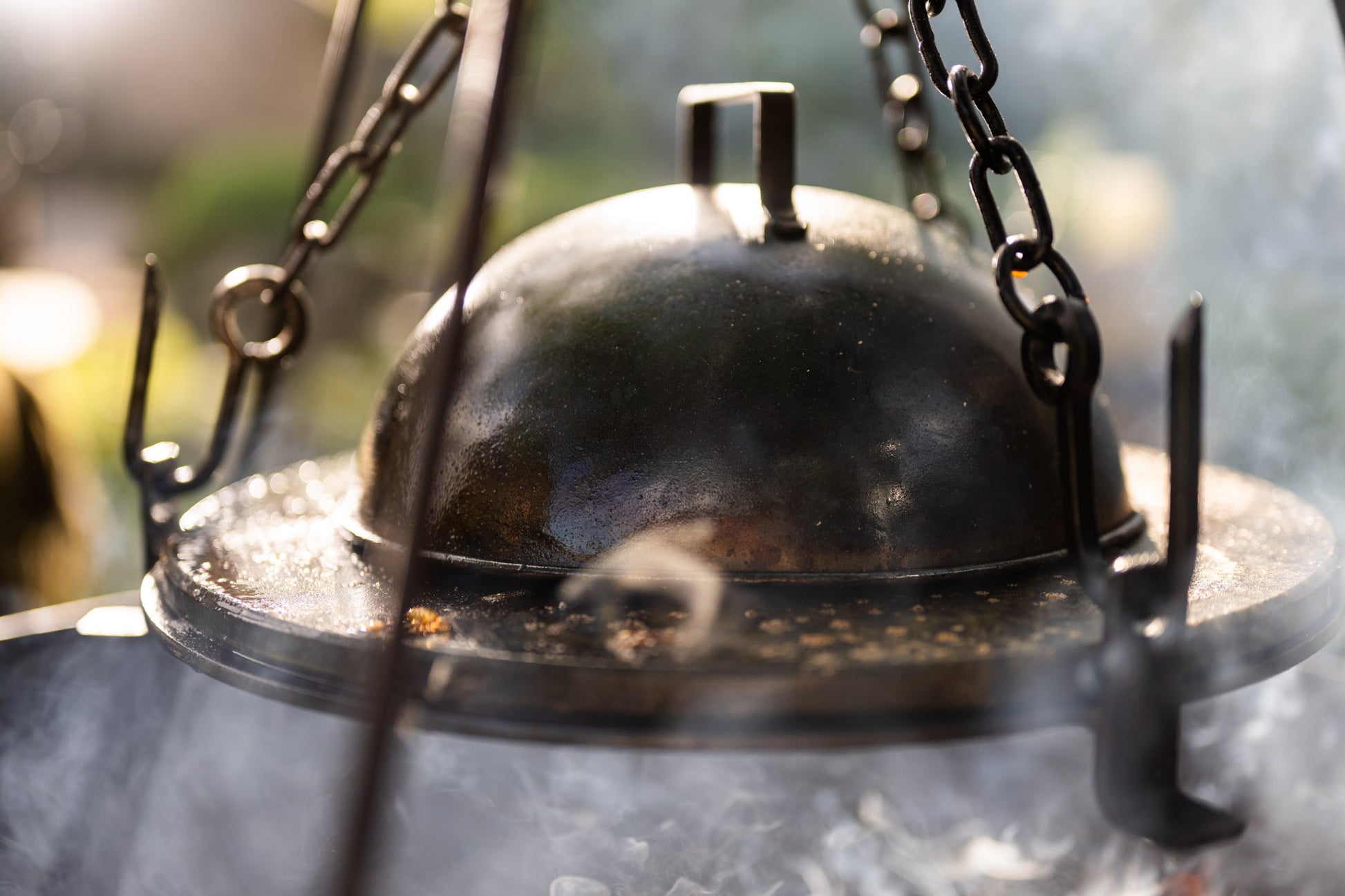 BBQ cloche cover trapping heat and smoke over a hot stone griddle plate above an outdoor fire pit.