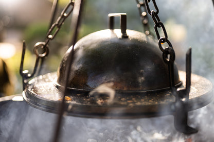 BBQ cloche cover trapping heat and smoke over a hot stone griddle plate above an outdoor fire pit.