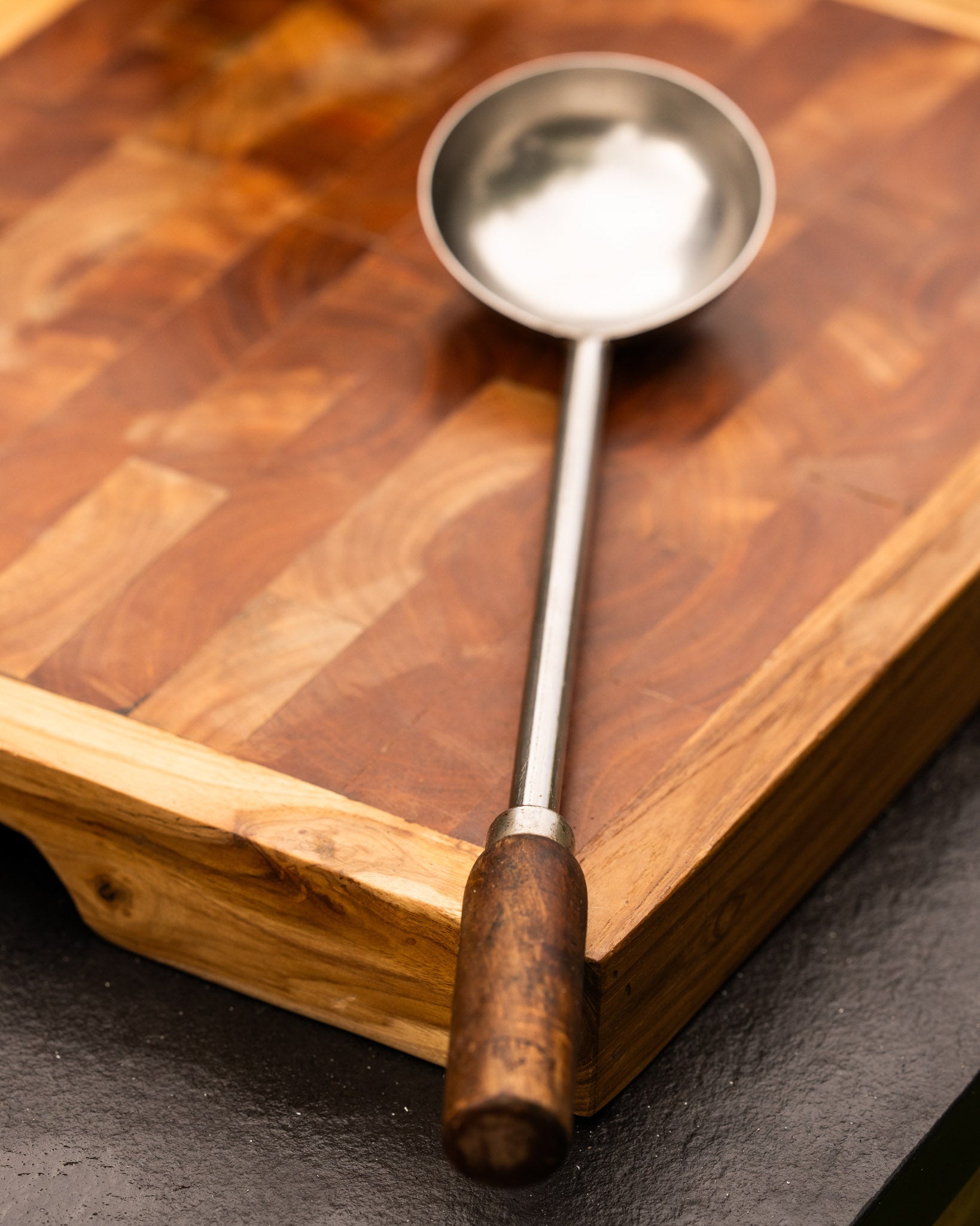 Metal ladle with wooden handle on a wooden cutting board