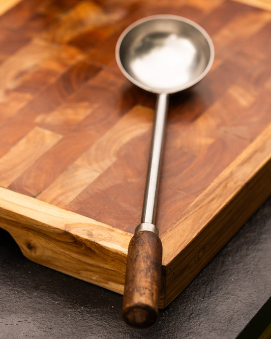 Metal ladle with wooden handle on a wooden cutting board