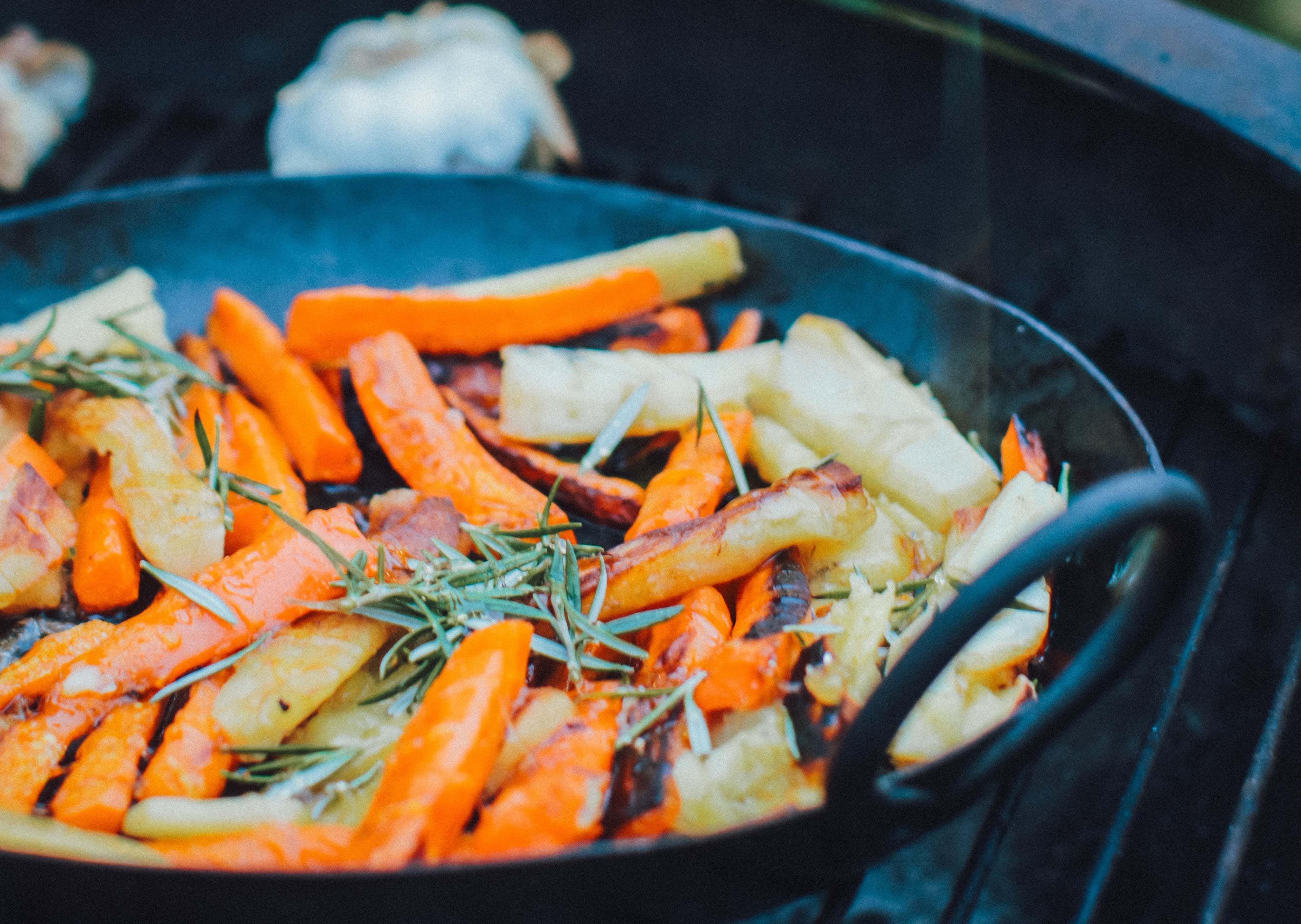 Carrots and parsnips cooking in a pan on a BBQ grill.