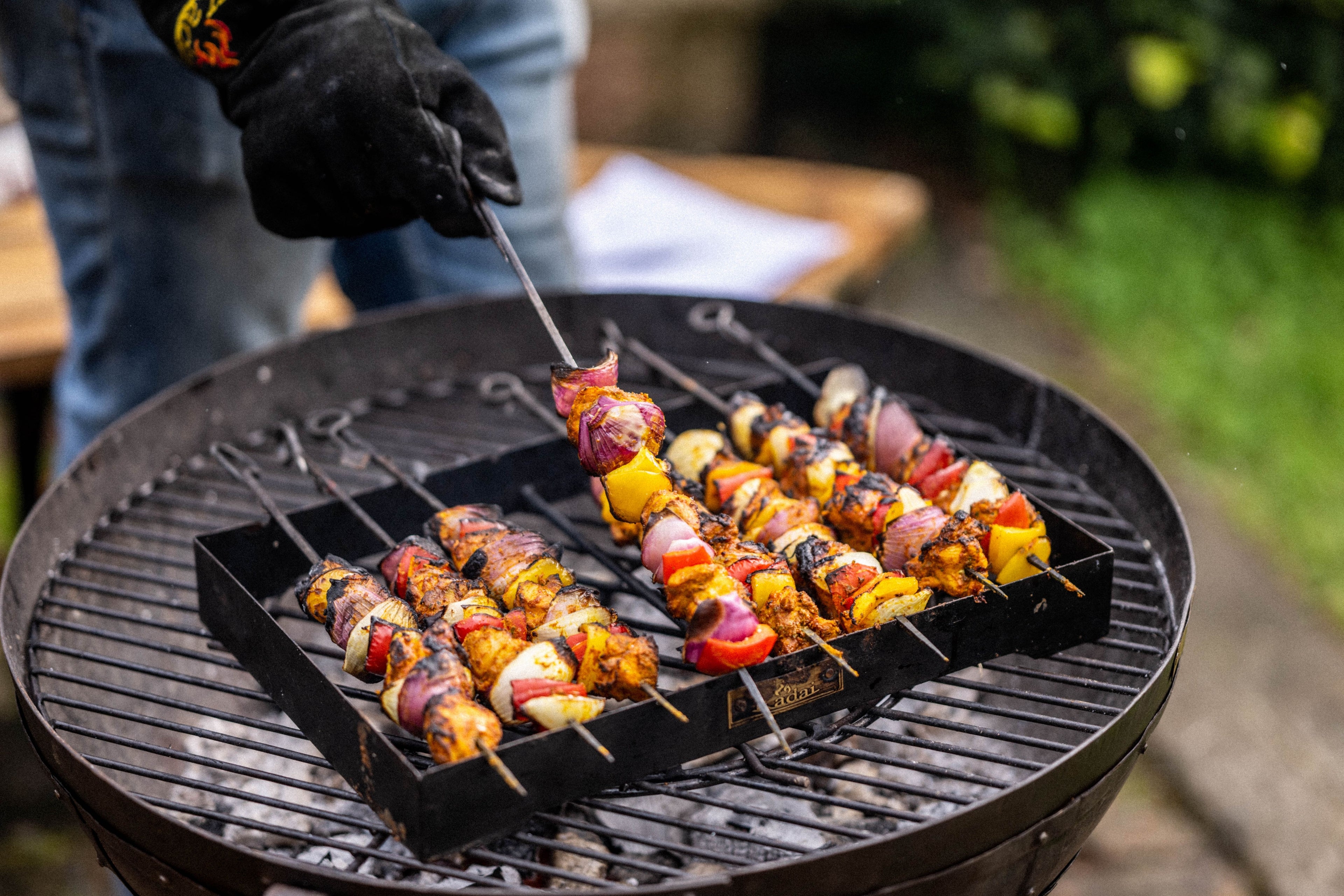 Outdoor barbecue skewers with chargrilled vegetables and marinated meat cooking on a metal rack over a Kadai fire bowl