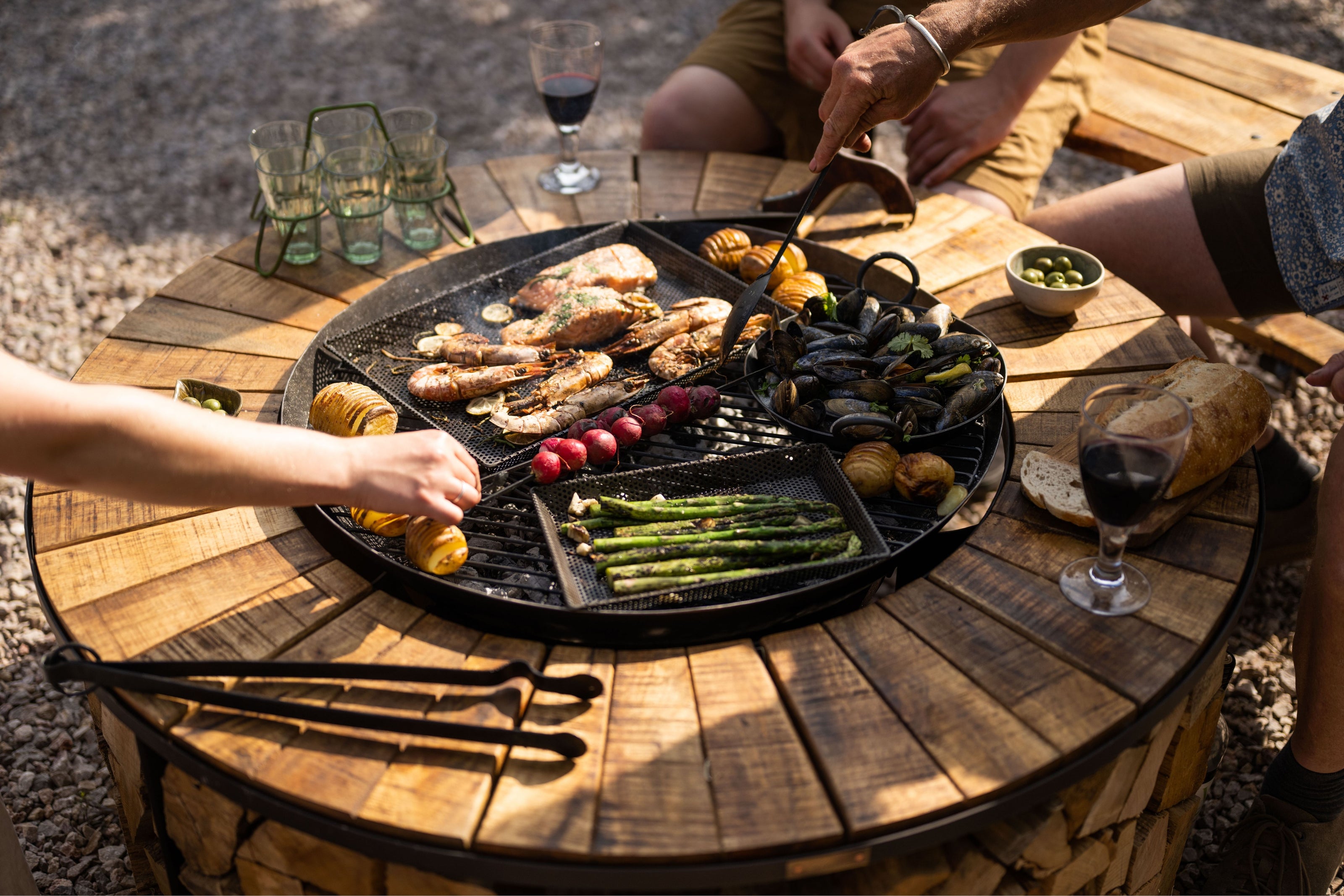 People sat around a bbq grill cooking and eating food.
