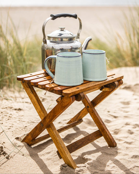 Tea kettle and mugs on a wooden stool with a beach background