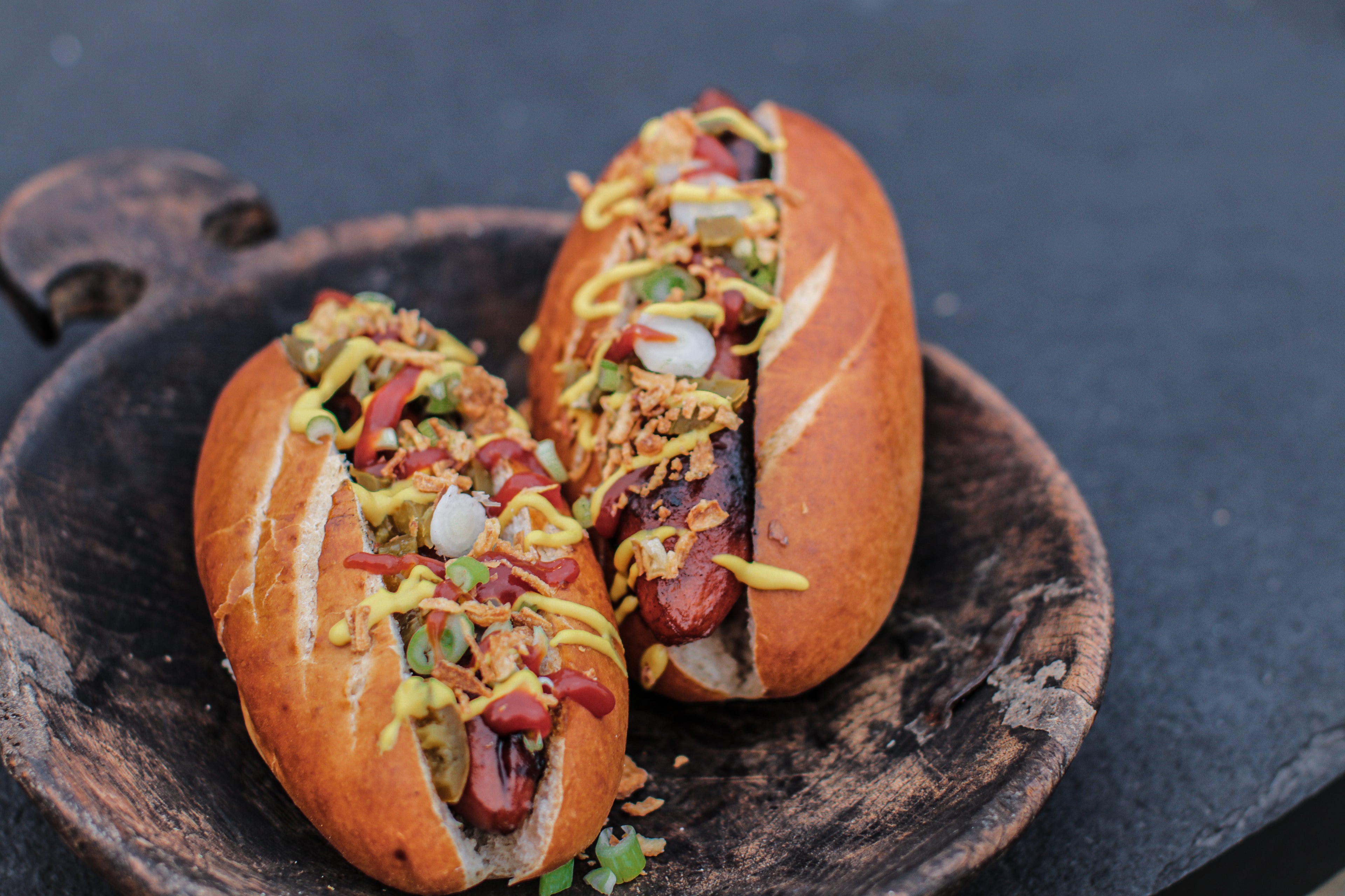 Two hot dogs with mustard and relish on a wooden plate.