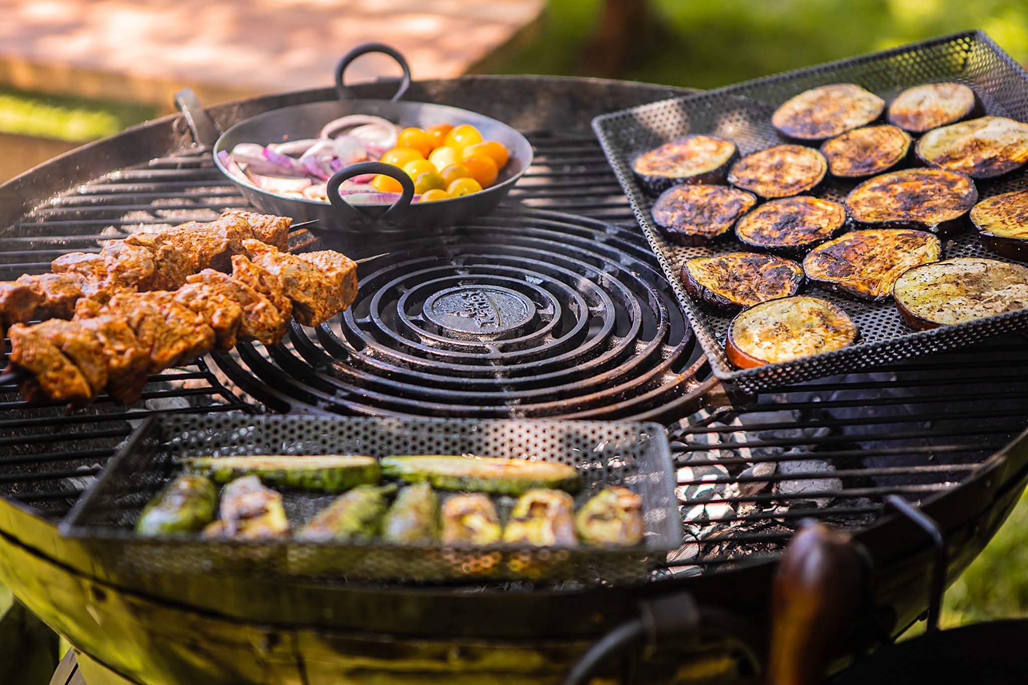Variety of meats and vegetables cooking on a circular stone griddle plate barbecue over hot coals outdoors