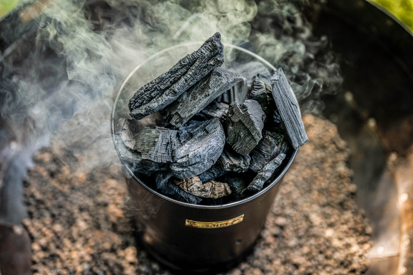 Close-up of a charcoal starter chimney packed with hot smoking charcoal ready for outdoor grilling and fire pit cooking