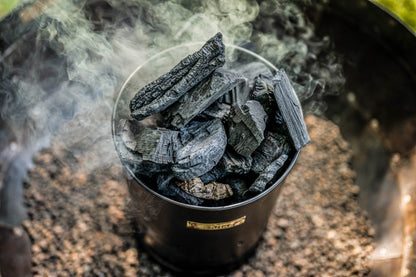 Close-up of a charcoal starter chimney packed with hot smoking charcoal ready for outdoor grilling and fire pit cooking
