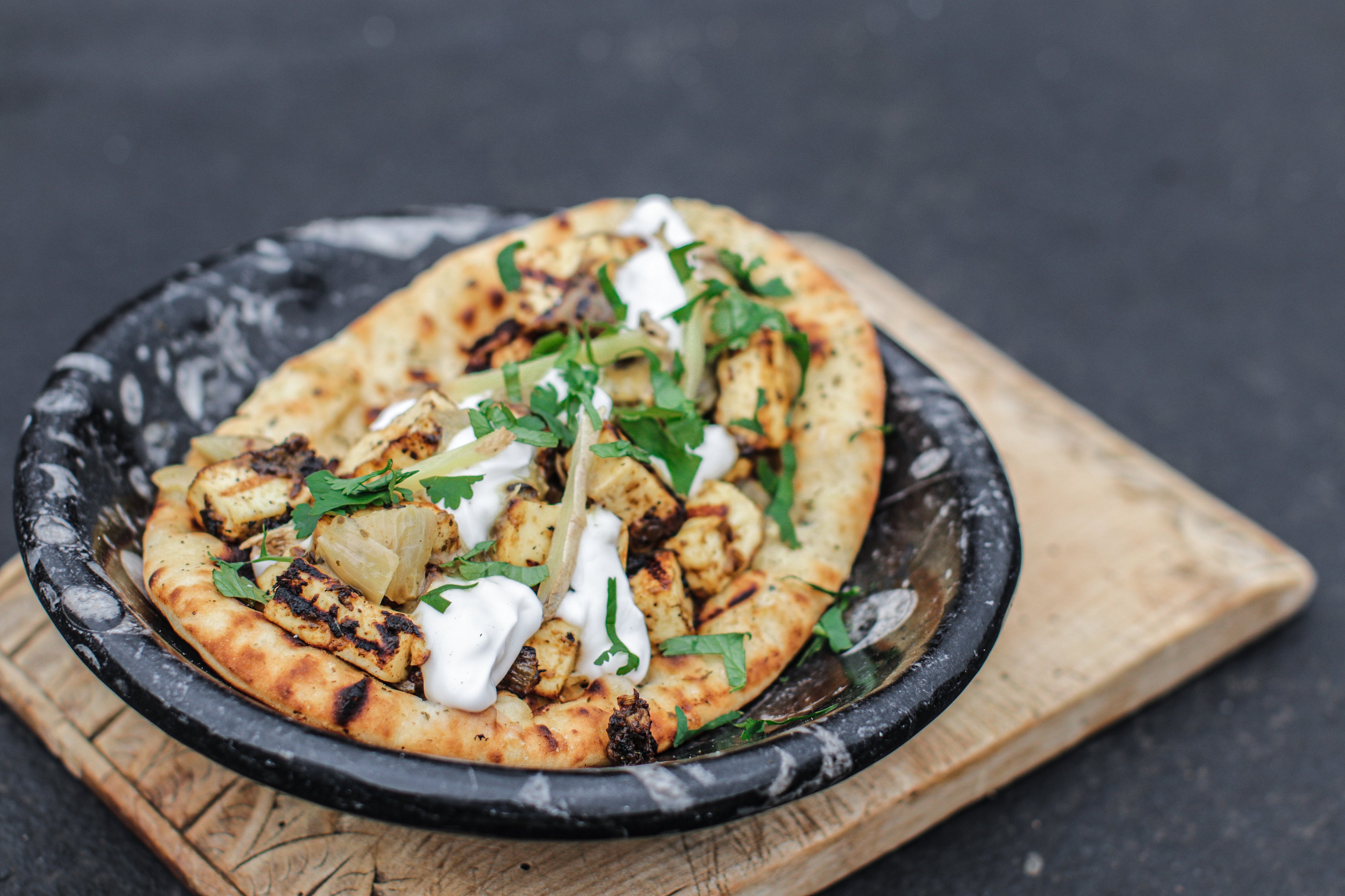 Small naan bread with paneer and yoghurt on a black plate with a dark background