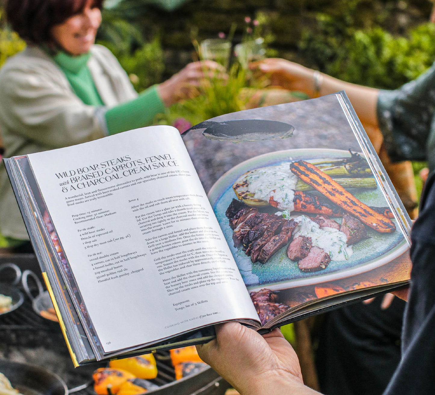 Open Kadai live fire cookbook showing steak recipe with grilled meat and vegetables beside outdoor barbecue