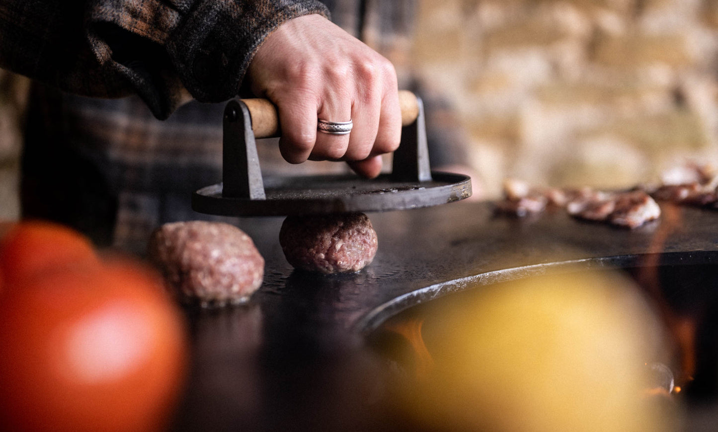 Person pressing raw beef patties with a burger press on a grill.