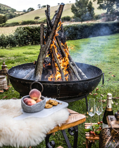kadai Fire pit with burning wood in a grassy outdoor setting